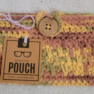 May include: Crocheted glasses pouch with a wooden button closure. The pouch is made in a multi-colored pattern of pink, yellow, and green. The tag reads "Glasses Pouch 100% Handmade".
