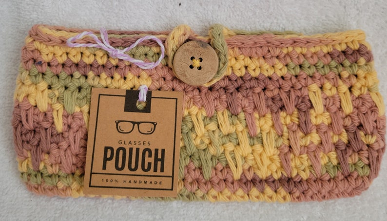 May include: Crocheted glasses pouch with a wooden button closure. The pouch is made in a multi-colored pattern of pink, yellow, and green. The tag reads "Glasses Pouch 100% Handmade".