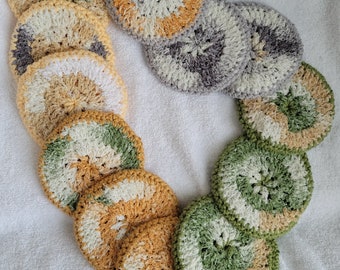 Op de afbeelding: Een set van tien gehaakte theedoeken in verschillende kleuren, waaronder geel, groen, wit en grijs. De theedoeken zijn in een cirkel op een witte handdoek gerangschikt.