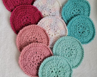 Op de afbeelding: Een set van negen gehaakte onderzetters in verschillende kleuren, waaronder roze, rood, teal en wit. De onderzetters zijn rond en hebben een textuur.