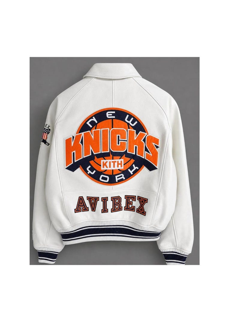 May include: A white varsity jacket featuring a large orange and navy blue New York Knicks basketball graphic on the back with the text KITH. The word AVIREX is embroidered below in navy blue. The cuffs and hem have navy blue and white stripes.