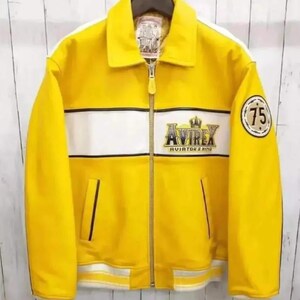 K&ouml;nnte beinhalten: Eine leuchtend gelbe Jacke mit einem wei&szlig;en horizontalen Bruststreifen und einem durchgehenden Rei&szlig;verschluss. Auf der Brust befindet sich ein gesticktes Avirex Aviator's King Logo mit Krone, am linken &Auml;rmel ein runder Aufn&auml;her mit der Zahl 75.