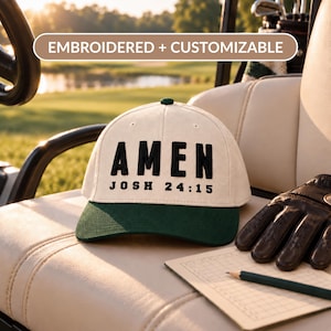 Könnte beinhalten: Eine cremefarbene Baseballkappe mit dunkelgrünem Schirm, die auf der Vorderseite den schwarzen gestickten Text AMEN und JOSH 24:15 aufweist. Über der Kappe befindet sich ein rechteckiges Etikett mit dem Text EMBROIDERED + CUSTOMIZABLE.