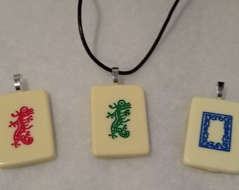 May include: Three white rectangular pendants with black cord necklaces. The pendants have different designs: a red dragon, a green dragon, and a blue square.