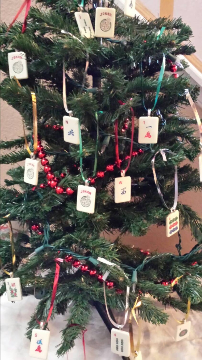 May include: A decorated Christmas tree with ornaments made from Mahjong tiles. The tiles are white with black and red symbols and hang from ribbons. Red bead garland and colorful ribbons add to the festive look.