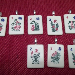 May include: A collection of eight rectangular pendants with silver-colored loops. Each pendant features a different design with Chinese characters and numbers. The designs include boats, landscapes, and floral motifs in red, green, and blue.