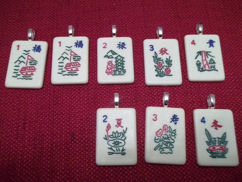 May include: A collection of eight rectangular pendants with silver-colored loops. Each pendant features a different design with Chinese characters and numbers. The designs include boats, landscapes, and floral motifs in red, green, and blue.