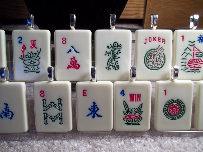 May include: A set of ten white ceramic mahjong tiles with green, red, and blue Chinese characters and symbols. The tiles are numbered 1, 2, 4, and 8, and include the characters "East", "South", "Win", and "Joker".