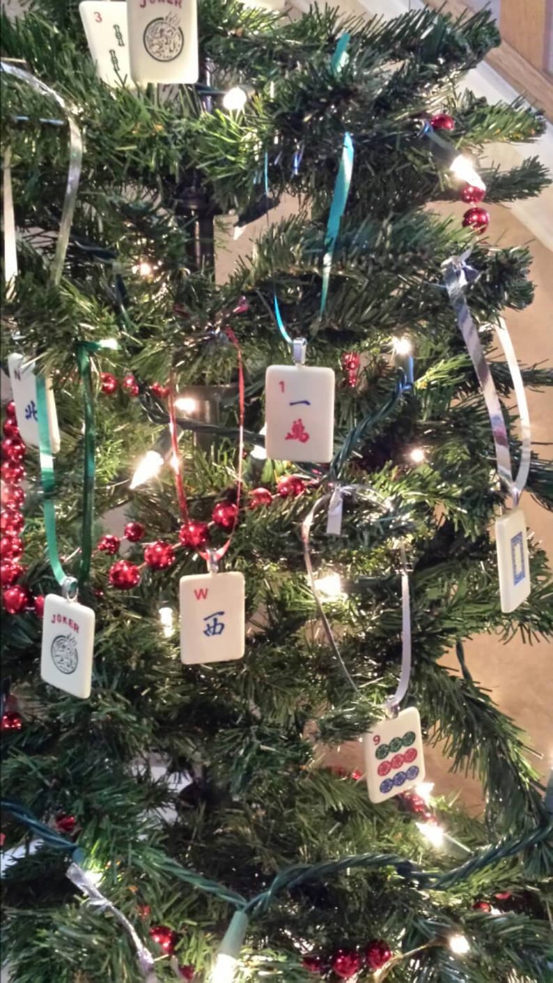 May include: A decorated Christmas tree with ornaments made from Mahjong tiles. The tree is adorned with red bead garlands, white lights, and silver and teal ribbons. The Mahjong tiles feature various symbols and characters.