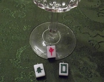 May include: Three white mahjong tiles with black and green characters and a red character on a green tablecloth. The tiles are hanging from a wine glass.