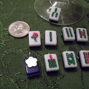 May include: Nine white ceramic tiles with green and red designs. The tiles are shaped like mahjong tiles and have different symbols on them. Some of the tiles have a flower design, while others have a geometric design.