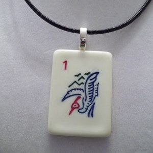 May include: A white ceramic pendant necklace with a black cord. The pendant is a rectangular tile with a blue and red bird design and the number "1" in the top left corner.