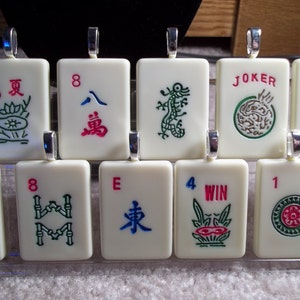 May include: A collection of rectangular, off-white pendants with silver-colored loops. Each pendant features a different design, including numbers, Chinese characters, and illustrations in various colors like red, green, and blue. Some pendants have the word "JOKER" and "WIN".
