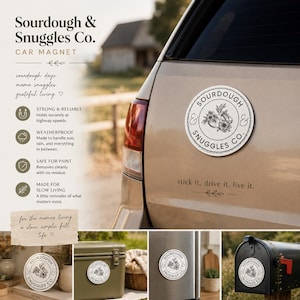 May include: A round white car magnet featuring a black circular border and the text Sourdough & Snuggles Co. surrounding a central botanical illustration of wheat and flowers. The magnet is displayed on a tan vehicle, a cooler, and a mailbox.