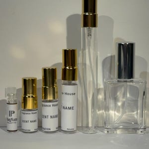 Peut inclure: Une collection de cinq flacons de parfum en verre transparent de tailles et formes vari&eacute;es. Quatre sont des fioles cylindriques avec des bouchons dor&eacute;s et des &eacute;tiquettes blanches indiquant Fragrance House, SCENT NAME et Volume.