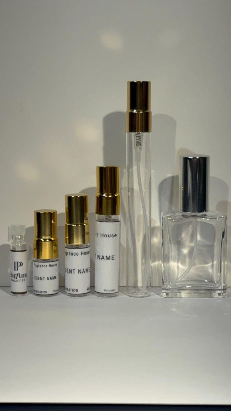 Peut inclure: Une collection de cinq flacons de parfum en verre transparent de tailles et formes vari&eacute;es. Quatre sont des fioles cylindriques avec des bouchons dor&eacute;s et des &eacute;tiquettes blanches indiquant Fragrance House, SCENT NAME et Volume.