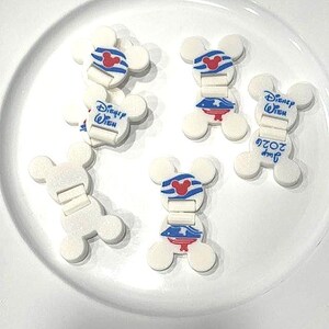 May include: A collection of white plastic cable clips shaped like Mickey Mouse heads. Some clips feature blue and white striped patterns with a red Mickey icon, while others display the blue text Disney Wish and the date July 2022 in blue ink.