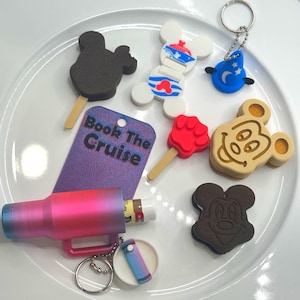May include: A collection of small items including a black mouse-shaped ice lolly, a white mouse-shaped figure, a blue wizard hat keyring, a red paw-shaped ice lolly, a tan mouse-shaped biscuit, a purple tag reading Book The Cruise, and a pink tumbler.