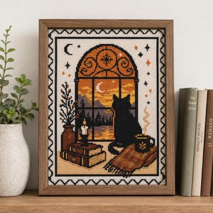 Puede incluir: Un bordado en punto de cruz enmarcado que representa un gato negro sentado junto a una ventana al atardecer. La escena incluye una luna creciente, una vela sobre libros apilados, una taza con vapor y una manta estampada en un borde.