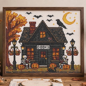 May include: A framed cross-stitch artwork depicting a dark house with the word BOOKS above the door. The scene includes skeletons sitting on pumpkins, a large orange tree, a yellow crescent moon, a black crow, and bats against a white background.