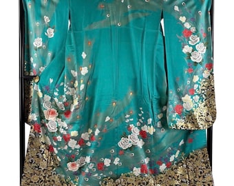 May include: A teal kimono with a floral pattern of white and red roses, displayed on a black stand. The bottom hem features a gold and black ornate design. The sleeves and body are adorned with scattered floral accents.