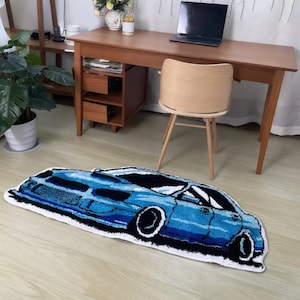May include: A tufted rug shaped like a sports car in shades of blue, black, and white. The rug features a detailed graphic design of a vehicle with prominent wheels, windows, and body lines, outlined in white against a dark blue and black interior.
