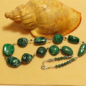 Peut inclure: Un collier de pierres vertes et blanches tachetées avec une chaîne et un fermoir argentés. Le collier est composé de grosses pierres de forme irrégulière.
