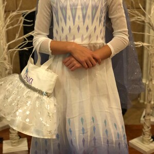 May include: A white and blue princess costume with a sparkly cape and a white tote bag with the name "Ava" embroidered on it.