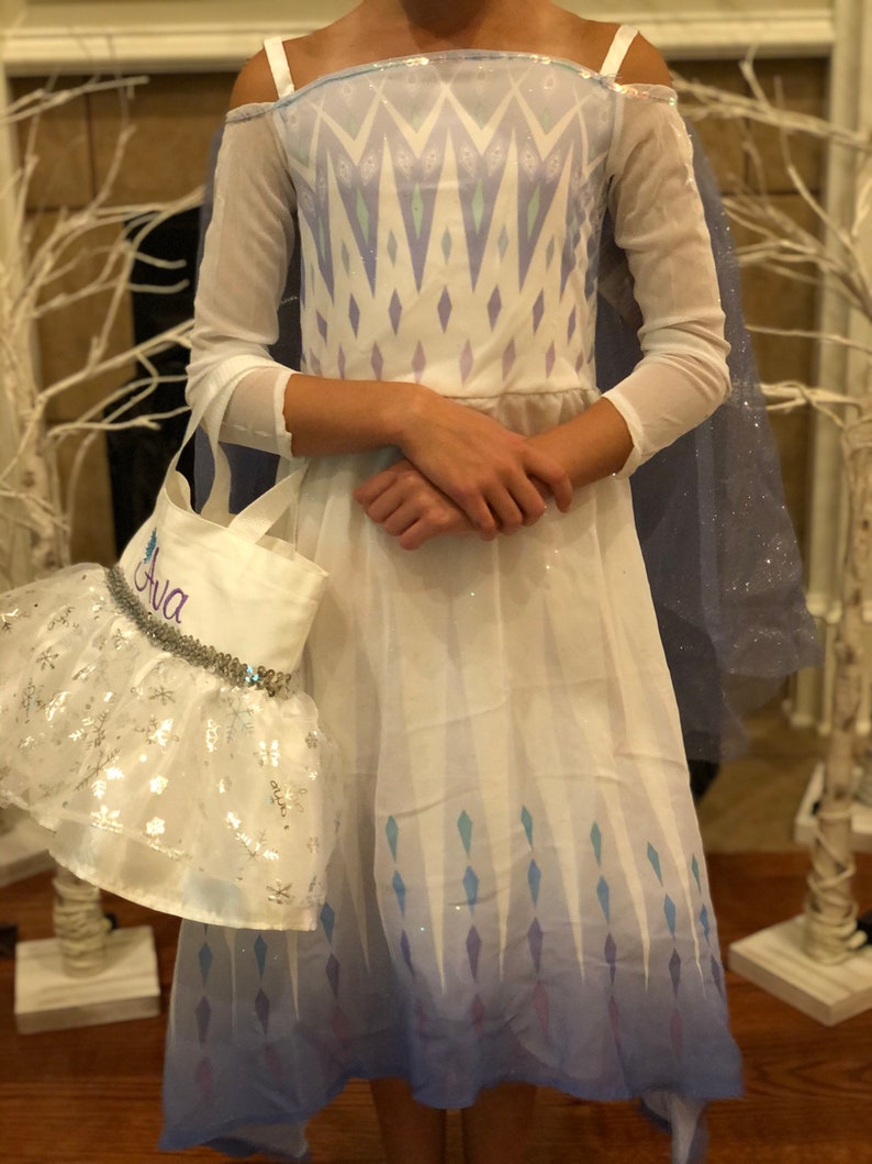 May include: A white and blue princess costume with a sparkly cape and a white tote bag with the name "Ava" embroidered on it.