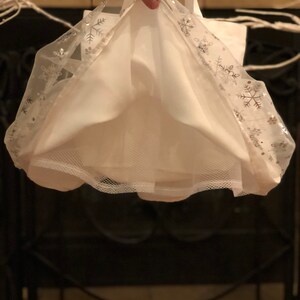 May include: White tulle skirt with silver snowflake trim. The skirt is gathered at the waist and has a mesh lining.