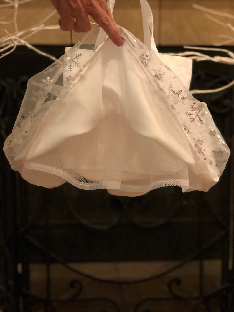 May include: White tulle skirt with silver snowflake trim. The skirt is gathered at the waist and has a mesh lining.