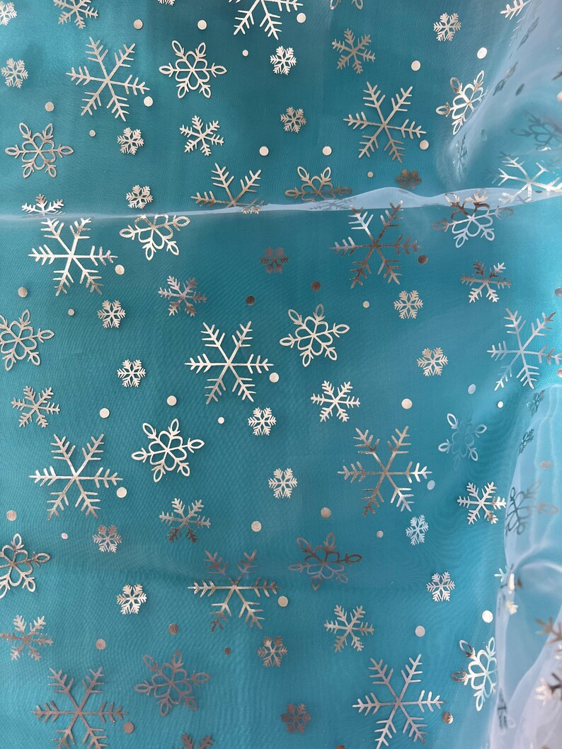Puede incluir: Una tela transparente de color turquesa con un patr&oacute;n repetido de copos de nieve plateados y peque&ntilde;os puntos. Los copos de nieve var&iacute;an en tama&ntilde;o y dise&ntilde;o, creando un aspecto invernal y festivo. La tela es ligeramente transl&uacute;cida.