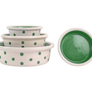 May include: A set of three round ceramic bowls stacked together and one separate bowl. The bowls are white with green polka dots on the exterior and have a solid green interior. Each bowl features a smooth, glossy finish and a wide, flat rim.