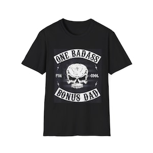 Puede incluir: Una camiseta negra de manga corta con un gráfico central de una calavera blanca. El texto dice ONE BADASS BONUS DAD con las palabras FUN y COOL a ambos lados de la calavera. El diseño incluye detalles de rayos y un fondo oscuro.