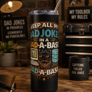 Könnte beinhalten: Ein schwarzer zylindrischer Becher mit transparentem Deckel und Metallstrohhalm. Die Außenseite zeigt eine Grafik mit dem Text "KEEP ALL MY DAD JOKES IN A DAD-A-BASE" sowie eine Illustration eines Computers, eines Datenbank-Symbols und eines bärtigen Gesichts.