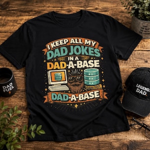 Könnte beinhalten: Ein schwarzes T-Shirt mit einem Aufdruck, der den Text I KEEP ALL MY DAD JOKES IN A DAD-A-BASE zeigt. Das Design umfasst einen Computermonitor, einen Stapel Datenträger und ein bärtiges Gesicht mit Sonnenbrille in Orange, Petrol und Weiß.