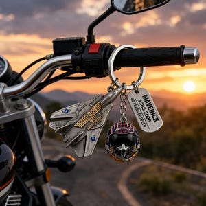May include: A silver Top Gun 40th Anniversary keychain set, including a fighter jet, pilot helmet, and a dog tag with "Maverick" and "40 Years of Speed" text. The keychains are attached to a motorcycle handlebar.
