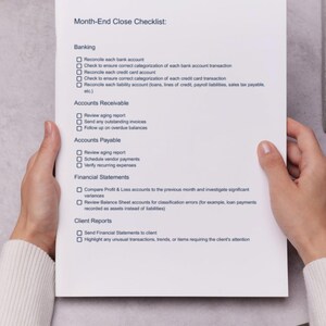 May include: A white paper titled "Month-End Close Checklist" is held by a person. The checklist includes sections for Banking, Accounts Receivable, Accounts Payable, Financial Statements, and Client Reports. The paper is on a gray surface.