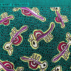 May include: A teal fabric featuring a repeating pattern of stylised white, purple, and magenta abstract creatures on a black speckled background. The top edge includes a green border with the text VERITABLE JAVA HOLLAND printed in white.
