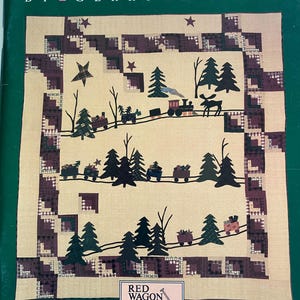 May include: A book cover titled FALL INTO WINTER BY GERRY KIMMEL featuring a quilt pattern with a train, pine trees, stars, and a moose on a beige background. A small box at the bottom displays a red wagon illustration with the text RED WAGON.