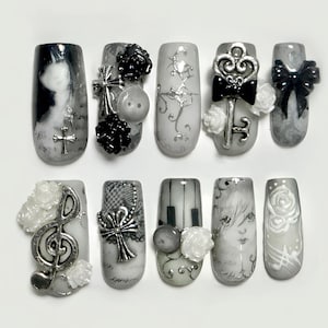 May include: A set of ten press-on nails featuring a monochrome color palette. Designs include silver cross charms, black and white 3D roses, a silver treble clef, a silver key, lace patterns, piano keys, and illustrated portraits on a gray background.
