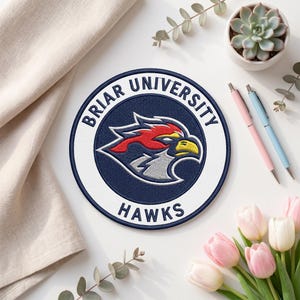 May include: A circular embroidered patch with the words "Briar University" and "Hawks" in white on a navy blue background. The patch has a white border and a central design of a red and yellow bird.