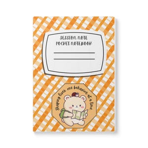 May include: A pocket notebook with an orange and white diagonal gingham pattern. The cover features a white label with the text SESSION NOTE POCKET NOTEBOOK and a hexagonal badge showing a cartoon bear with a map and the text Shaping lives, one behavior at a time.