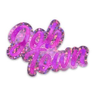 May include: A die-cut sticker featuring the text Job Town in a bold, cursive font. The lettering has a vibrant pink and purple watercolour texture, while the background of the sticker displays a shimmering, holographic glitter pattern.