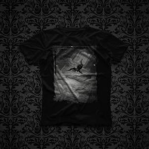 May include: A black short-sleeved t-shirt featuring a rectangular graphic print on the chest. The print depicts a monochromatic scene of a winged figure falling through a cloudy sky with rays of light shining down from above, set against a dark background.