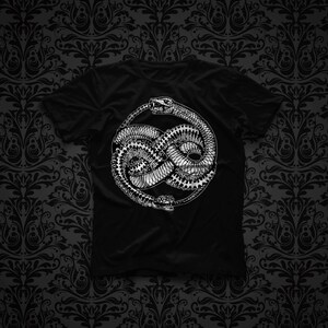 Könnte beinhalten: Ein schwarzes Kurzarm-T-Shirt mit einem weißen Grafikdruck einer Schlange, die sich zu einem kreisförmigen Knoten windet. Die Schlange ist mit detaillierten Schuppen und geöffnetem Maul dargestellt und bildet ein durchgehendes Motiv.