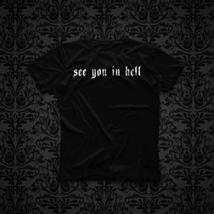 Pode incluir: Uma t-shirt preta de manga curta com o texto branco "see you in hell" impresso no peito numa fonte de estilo gótico. A peça tem um decote redondo e um corte padrão, apresentando uma cor preta sólida em todo o tecido.