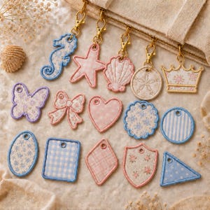 Puede incluir: Una colección de dijes de tela en varias formas, incluyendo un caballito de mar, estrella de mar, concha, corona, mariposa, lazo, corazón y formas geométricas, con patrones en tonos pastel y bordes cosidos.