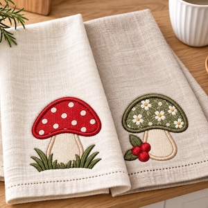 Puede incluir: Dos servilletas de lino beige claro con diseños de setas bordadas. Una servilleta muestra una seta roja con puntos blancos sobre hierba verde, mientras que la otra presenta una seta verde con flores blancas y bayas rojas.