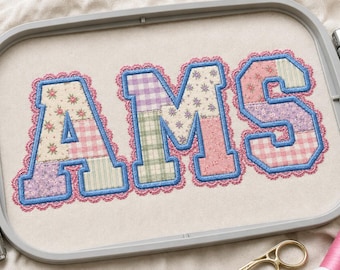 May include: The letters AMS are embroidered in a varsity font on a light fabric within a gray embroidery hoop. Each letter features a patchwork of floral, plaid, and gingham patterns in pastel colors, outlined in blue thread with a pink scalloped edge.